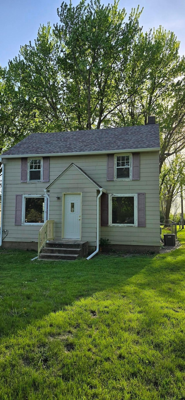 view of front facade featuring a front yard, a chimney, and cooling unit