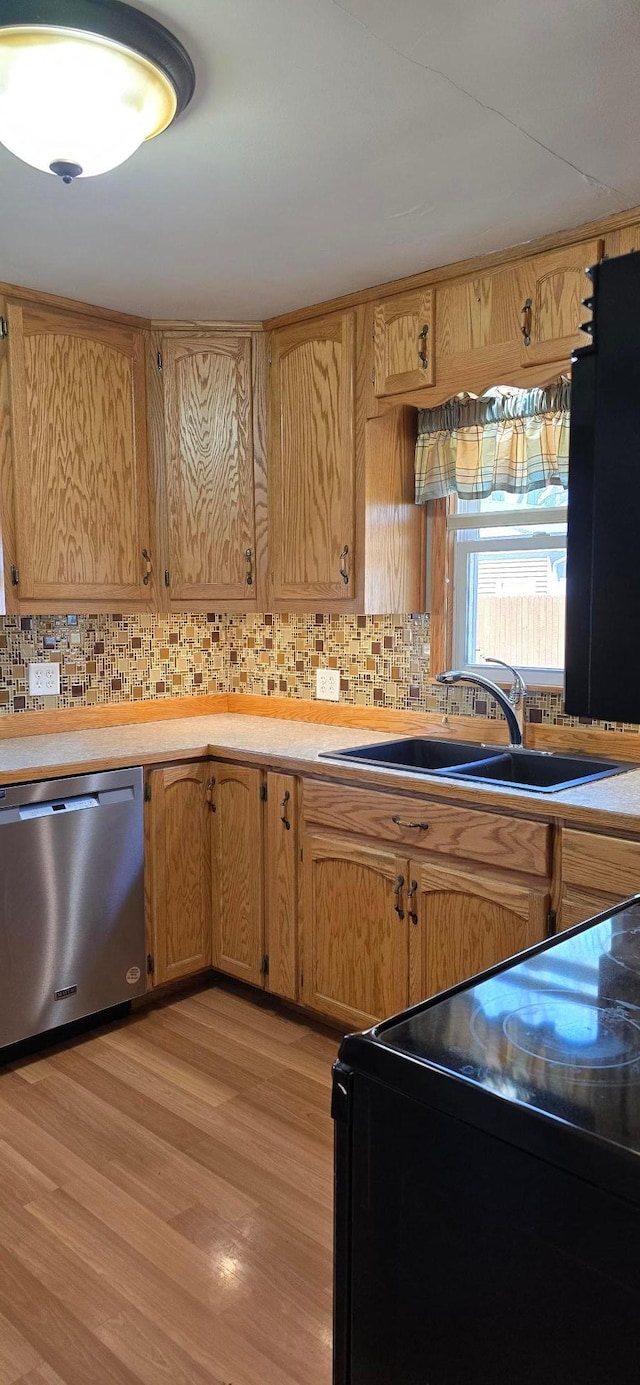 kitchen with stainless steel dishwasher, black electric range oven, a sink, decorative backsplash, and light wood finished floors