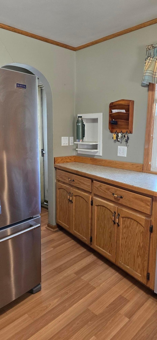 kitchen featuring freestanding refrigerator, ornamental molding, arched walkways, light wood finished floors, and light countertops
