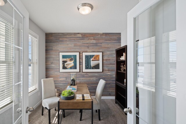 office with an accent wall, carpet flooring, french doors, wood walls, and baseboards