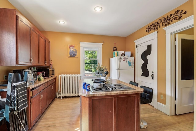 kitchen with light wood finished floors, stainless steel appliances, light countertops, a kitchen island, and radiator heating unit
