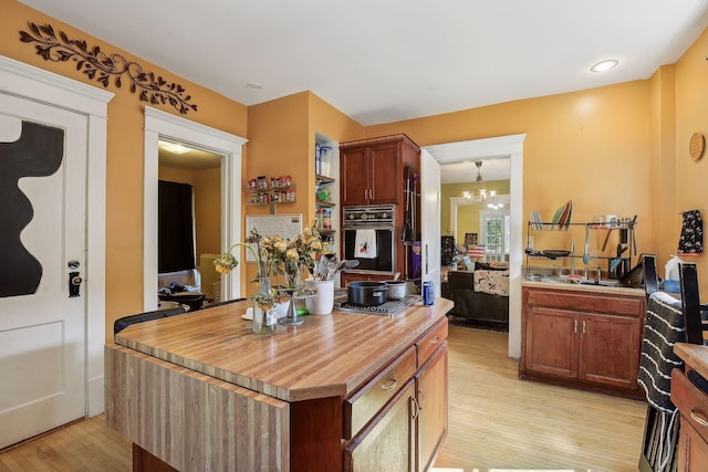 kitchen with wooden counters, a center island, a notable chandelier, light wood-style floors, and stainless steel oven