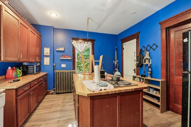 kitchen featuring light wood finished floors, a center island, stainless steel microwave, butcher block counters, and radiator heating unit