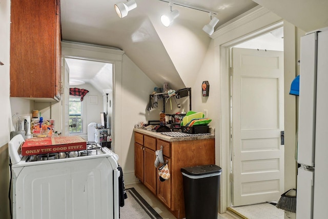 kitchen with freestanding refrigerator, washer / clothes dryer, brown cabinetry, track lighting, and vaulted ceiling