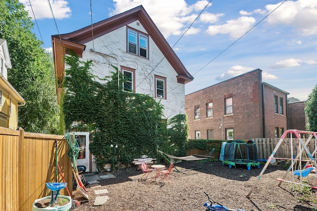 back of house featuring a playground, a fenced backyard, and stucco siding