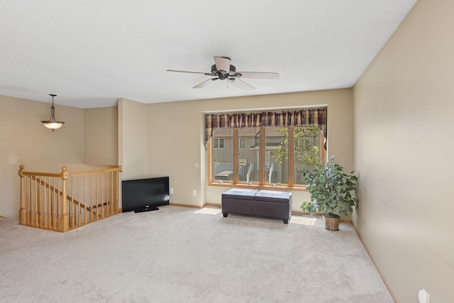 living area featuring an upstairs landing, ceiling fan, carpet floors, and baseboards