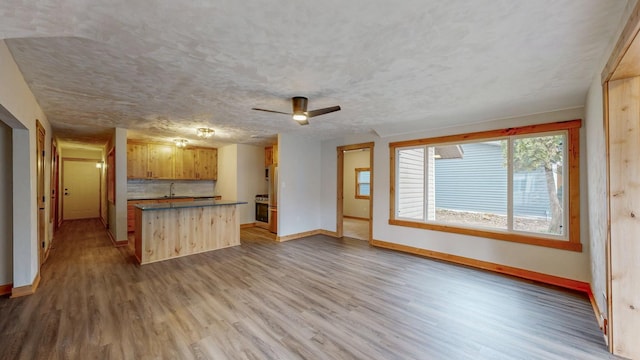 kitchen featuring baseboards, wood finished floors, open floor plan, a ceiling fan, and dark countertops