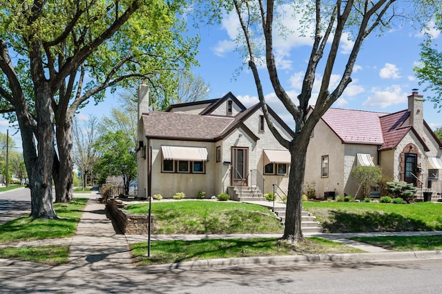 tudor house featuring a chimney, stucco siding, and a front lawn