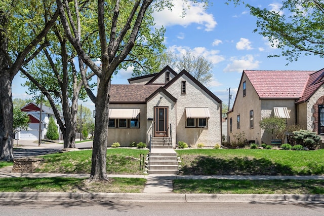 english style home with stucco siding and a front yard