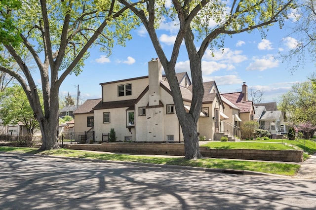 tudor-style house featuring stucco siding, a residential view, a chimney, and central AC