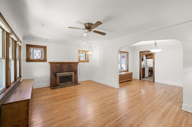 unfurnished living room with arched walkways, plenty of natural light, radiator heating unit, and a ceiling fan