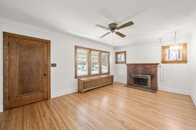 unfurnished living room featuring radiator heating unit, light wood-style floors, a fireplace, baseboards, and ceiling fan