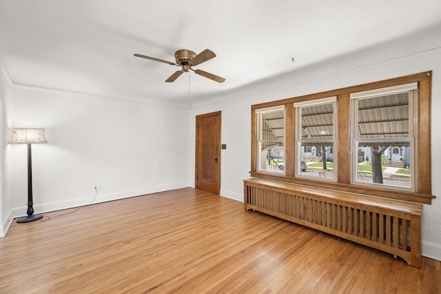 unfurnished room featuring radiator, wood finished floors, ceiling fan, and baseboards