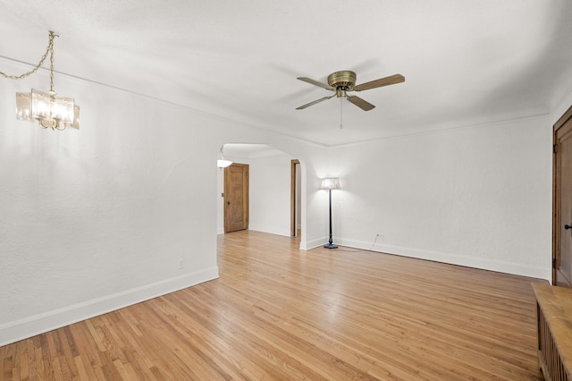 unfurnished living room with arched walkways, ceiling fan, baseboards, light wood-style floors, and a chandelier