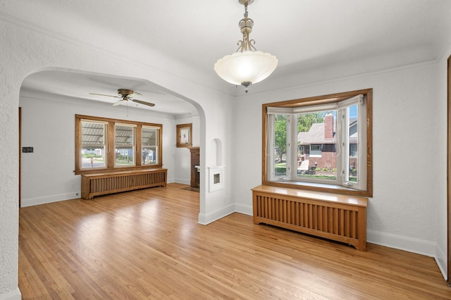 empty room featuring radiator heating unit, arched walkways, light wood-type flooring, and a ceiling fan