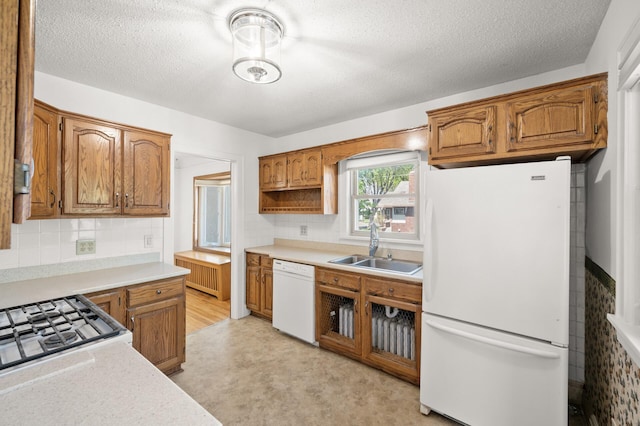 kitchen with white appliances, a sink, light countertops, brown cabinets, and a textured ceiling