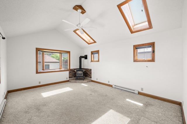 unfurnished living room featuring baseboard heating, a skylight, a wood stove, carpet, and lofted ceiling