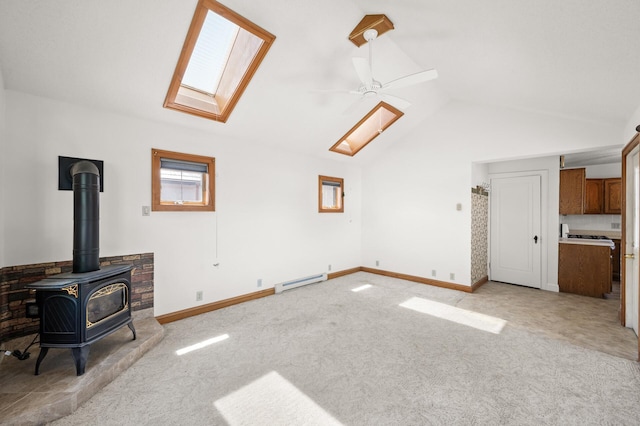 unfurnished living room featuring a baseboard radiator, a skylight, lofted ceiling, a wood stove, and light colored carpet