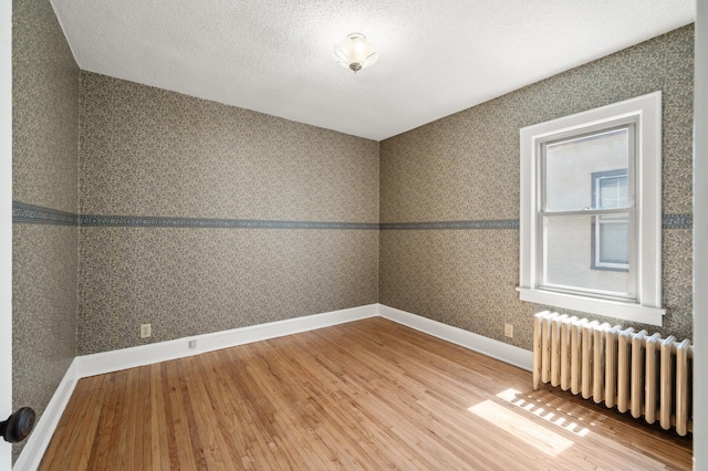 empty room with radiator heating unit, wood finished floors, baseboards, and a textured ceiling