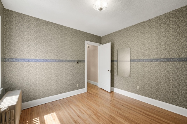 unfurnished room with hardwood / wood-style flooring, radiator heating unit, and baseboards