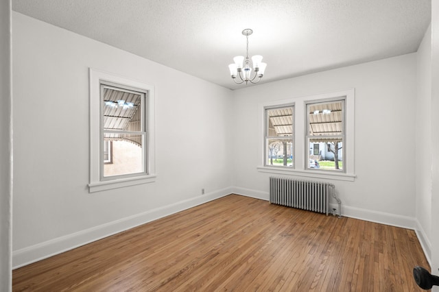 spare room with radiator heating unit, a chandelier, healthy amount of natural light, and wood-type flooring