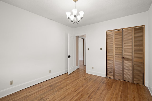 unfurnished bedroom featuring a chandelier, light wood-type flooring, baseboards, and a closet