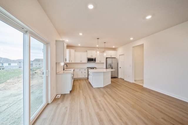 kitchen featuring light wood-style flooring, stainless steel appliances, a center island, a sink, and light countertops