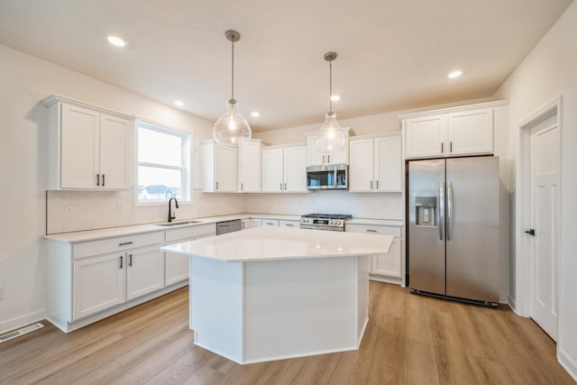 kitchen featuring appliances with stainless steel finishes, a sink, light countertops, tasteful backsplash, and light wood-type flooring