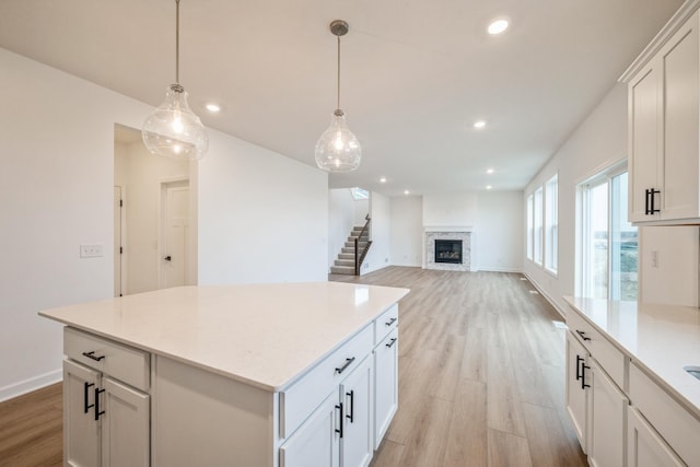 kitchen with light wood-style flooring, white cabinetry, a stone fireplace, and recessed lighting