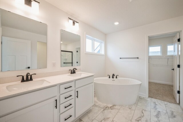 full bath featuring a sink, double vanity, a soaking tub, and marble finish floor