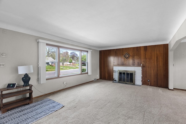 unfurnished living room with wood walls, light carpet, baseboards, and a fireplace with flush hearth