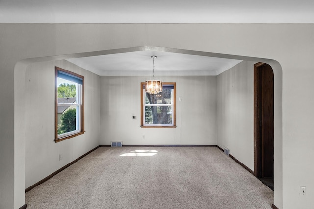 carpeted spare room featuring a chandelier, baseboards, and arched walkways
