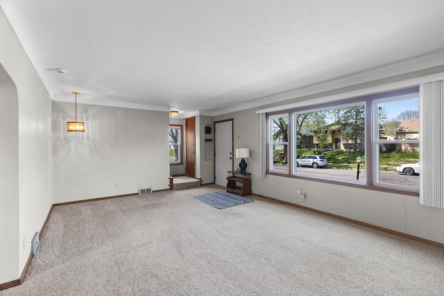 unfurnished living room featuring carpet flooring, healthy amount of natural light, a chandelier, and baseboards