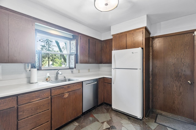 kitchen featuring freestanding refrigerator, stainless steel dishwasher, a sink, light countertops, and dark stone finish flooring