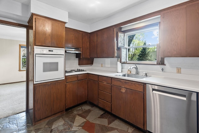 kitchen with white appliances, a sink, light countertops, decorative backsplash, and dark stone finish floors