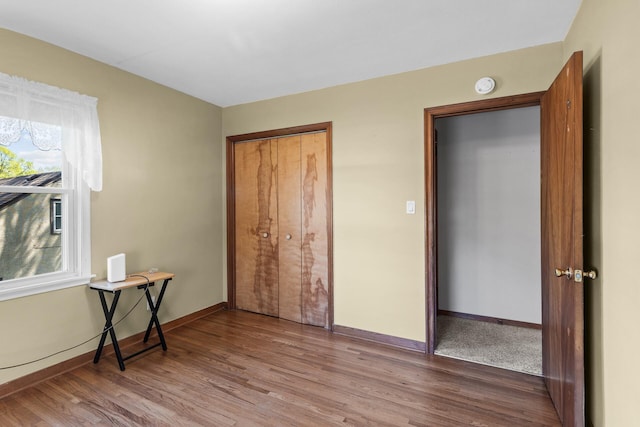 unfurnished bedroom featuring wood finished floors, baseboards, and a closet