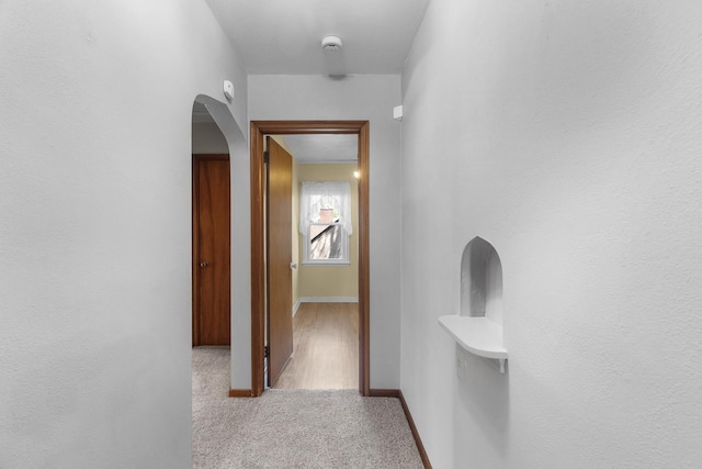 hallway featuring carpet flooring, arched walkways, and baseboards