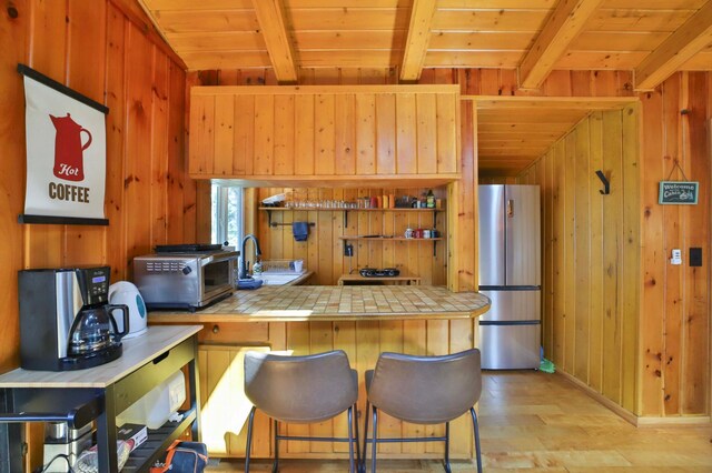 kitchen with freestanding refrigerator, wood walls, beamed ceiling, light wood-style flooring, and tile countertops