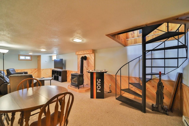 basement featuring wood walls, a wood stove, carpet flooring, stairs, and a wainscoted wall