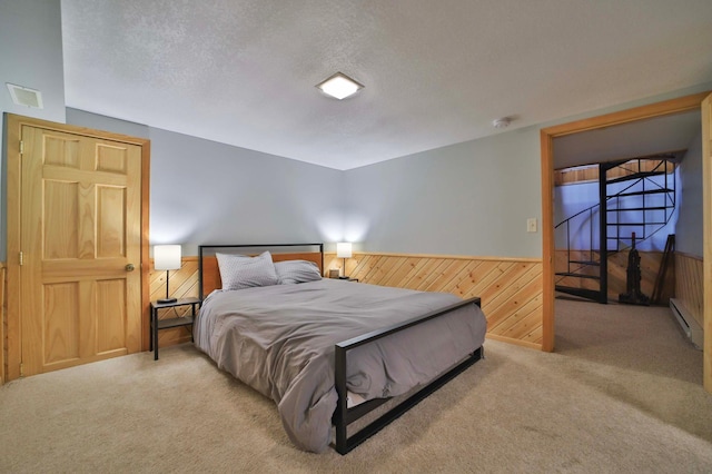 carpeted bedroom with a baseboard radiator, wooden walls, a textured ceiling, and a wainscoted wall