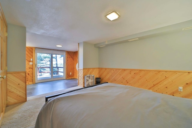 carpeted bedroom featuring wood walls, access to exterior, and a wainscoted wall
