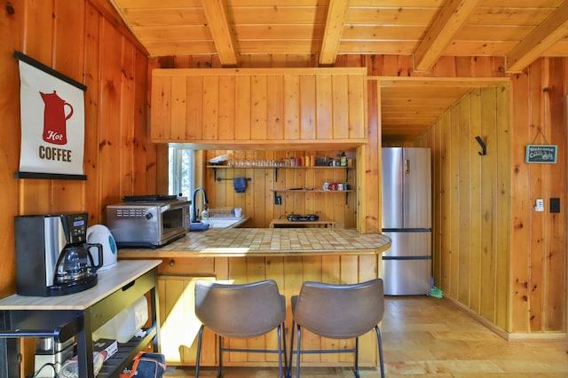 2202 Pine View Blvd, Motley, MN 56466 - kitchen with freestanding refrigerator, wooden walls, light wood-style flooring, tile counters, and a peninsula