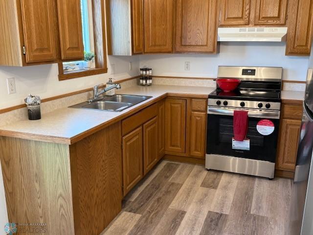 408 Np Ct, Breckenridge, MN 56520 - kitchen featuring under cabinet range hood, stainless steel range with electric cooktop, a sink, brown cabinetry, and light countertops