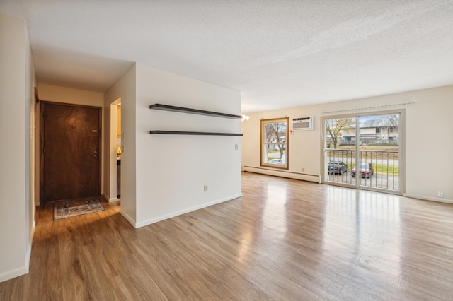 923 11th Ave S Unit 8, Hopkins, MN 55343 - unfurnished living room featuring baseboard heating, a wall unit AC, wood finished floors, baseboards, and a textured ceiling