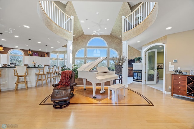 4126 Timberline Dr S, Fargo, ND 58104 - living area featuring light wood finished floors, ceiling fan, a glass covered fireplace, a high ceiling, and decorative columns