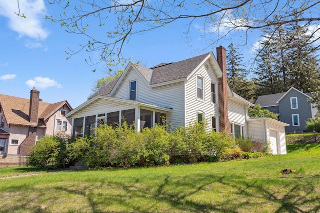 view of property exterior with a sunroom, a lawn, a chimney, and a garage