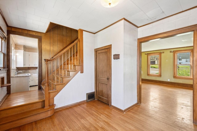 entrance foyer with light wood-style flooring, stairs, baseboards, and wood walls