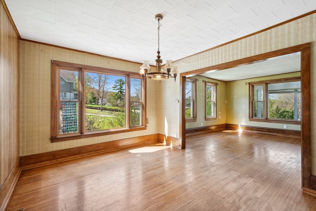 unfurnished dining area featuring a chandelier, ornamental molding, wood-type flooring, baseboards, and wallpapered walls