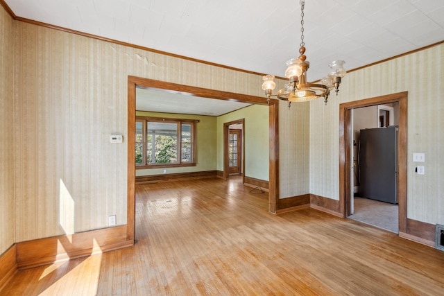 unfurnished room with hardwood / wood-style floors, a chandelier, ornamental molding, wallpapered walls, and baseboards