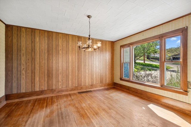 unfurnished dining area with a chandelier, hardwood / wood-style flooring, wooden walls, baseboards, and ornamental molding